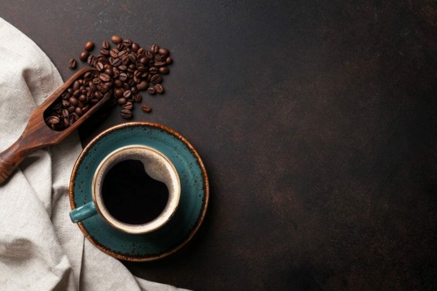 Black coffee in a cup next to a side of coffee beans