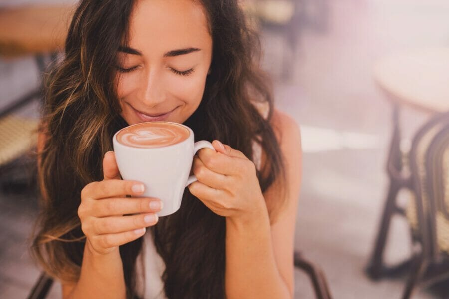 Young beautiful happy woman with long curly hair enjoying cappuccino in a cafe