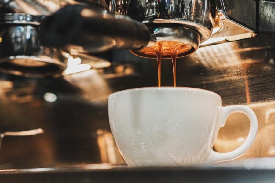 A photograph of espresso extraction from an espresso machine into a small white espresso cup.