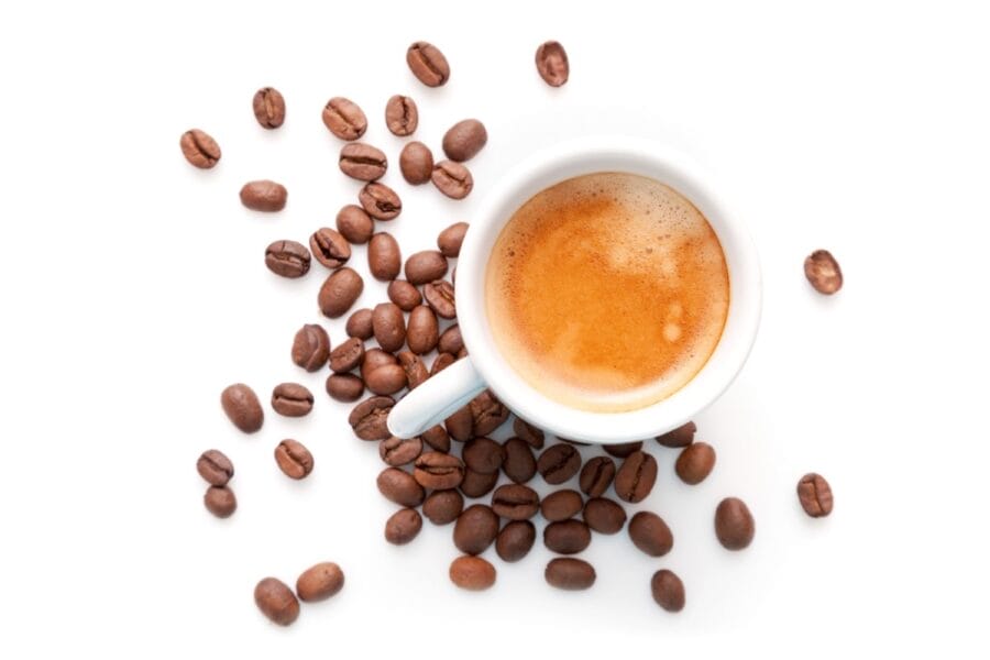 Whole medium roast coffee beans surround a small cup of brewed espresso