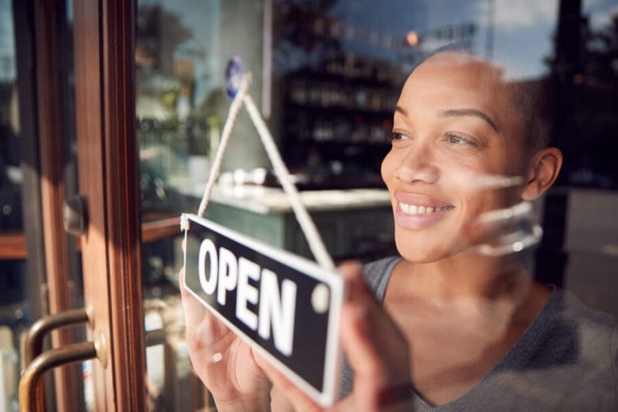 A female owner of a start up coffee franchise turns her closed sign in the window to open