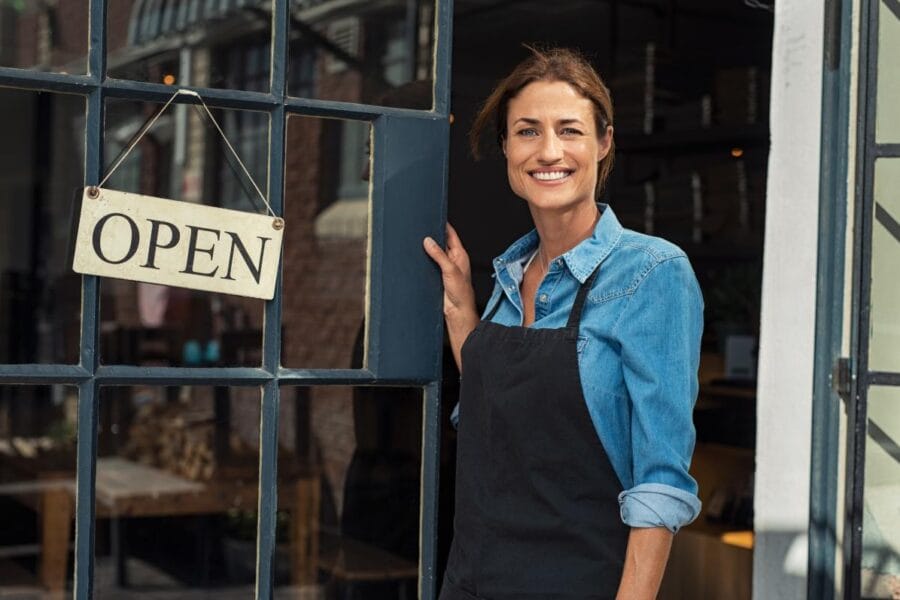 A woman standing in front of an open coffee shop.